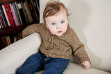 A baby sitting on a cream colored arm chair, modeling a brown button up raglan neckline front range sweater.
