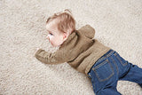 A baby in a brown raglan neckline sweater propping up from the floor with hands to show the back of the front range sweater.